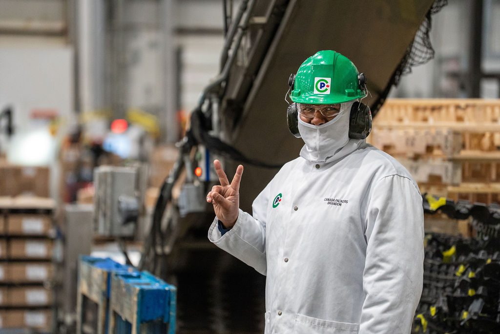 A person in PPE at the Canada Packers Brandon plant giving the piece sign